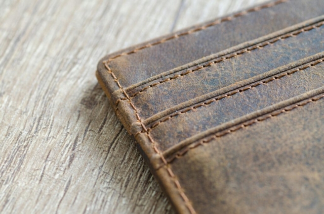 Detailed shot of a brown leather wallet on a textured wooden surface, showcasing stitching.